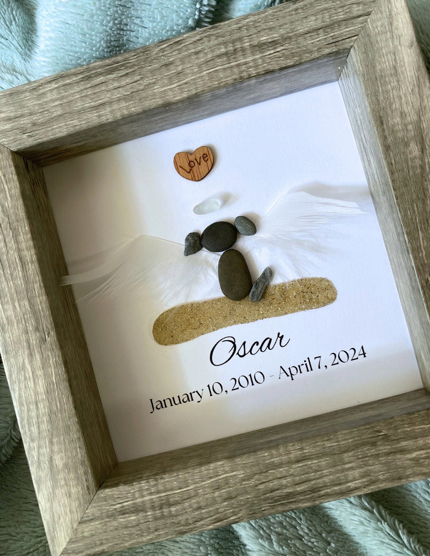 A personalized dog memorial gift featuring a white sea glass and pebble design with the name 'Oscar' and birth and death dates on a shadowbox frame.