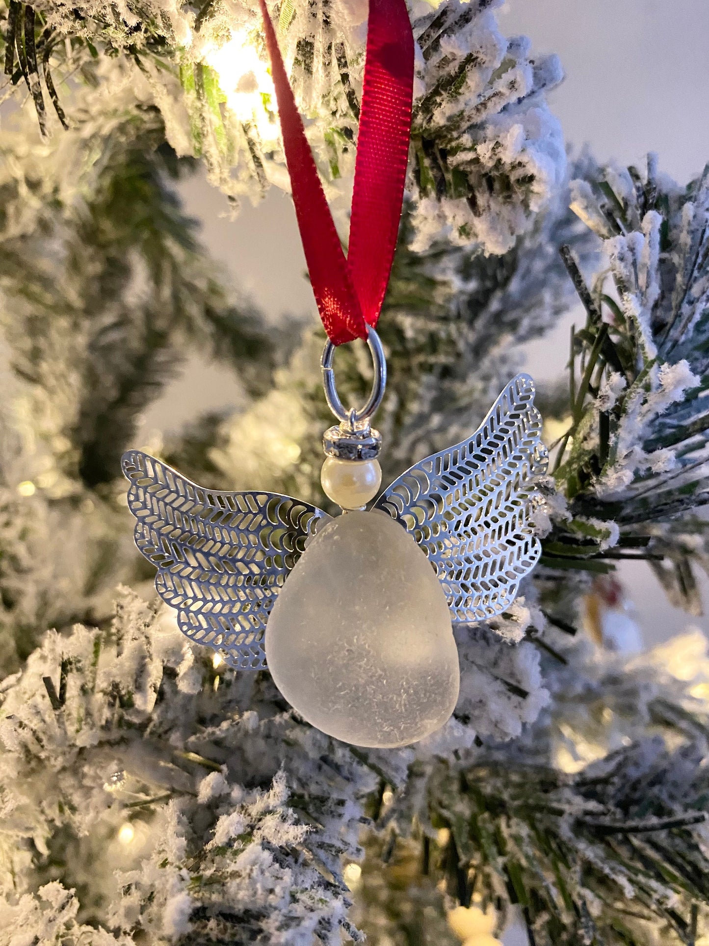 A handcrafted sea glass angel Christmas ornament with a red ribbon, displayed on a christmas tree