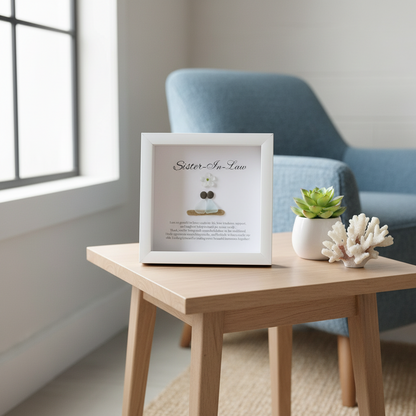 A framed personalized sea glass art piece with the inscription 'Sister-in-Law' on top, a white flower, and two  sea glass figures representing the sisters-in-law. The artwork is enclosed in a white frame.