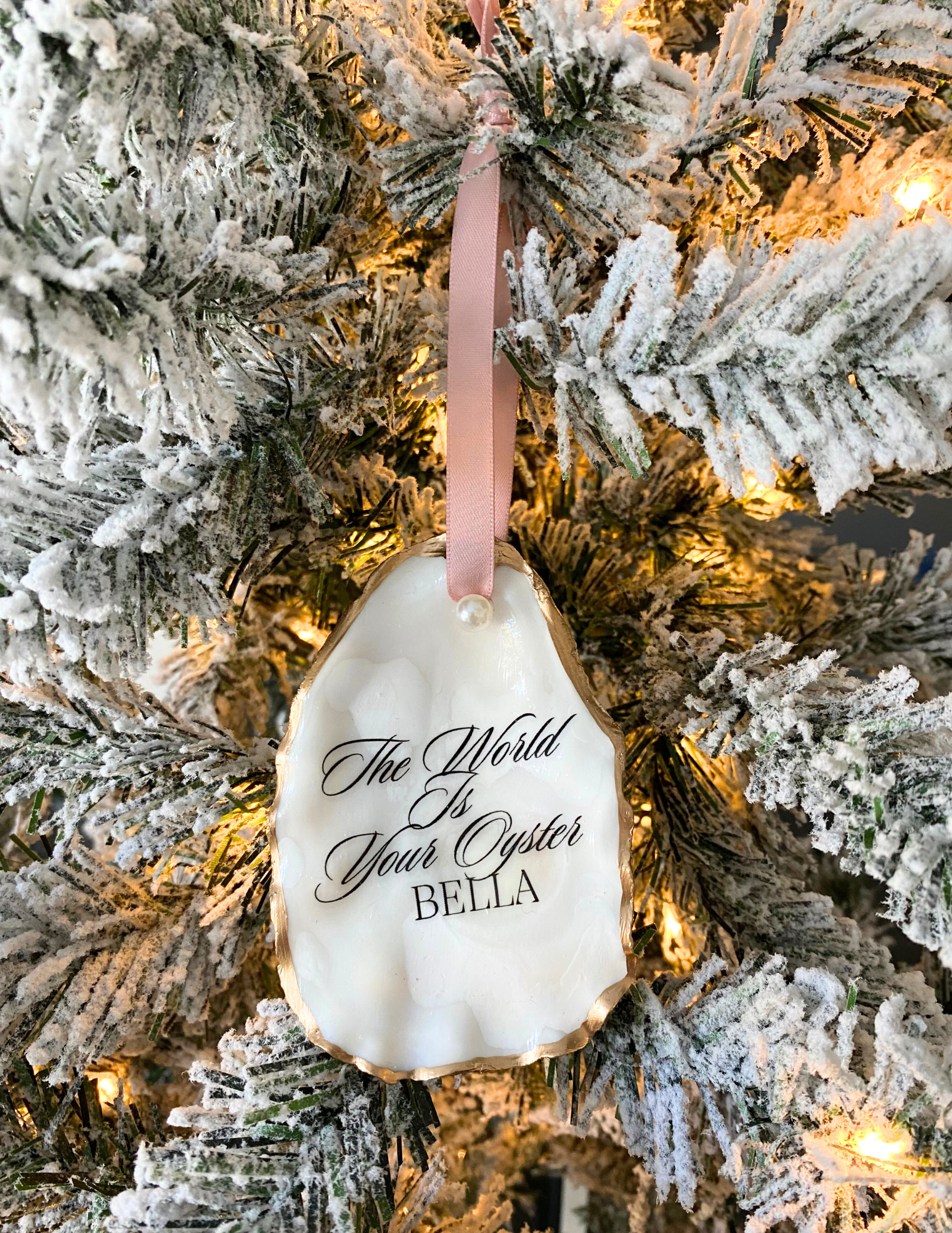 the world is your oyster ornament with gold gild trim pink ribbon and pearl hanging on a christmas tree