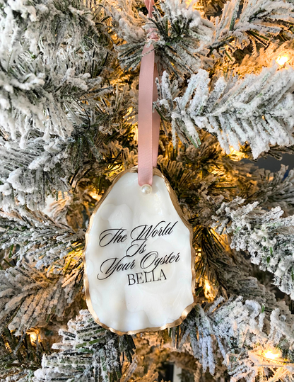 the world is your oyster ornament with gold gild trim pink ribbon and pearl hanging on a christmas tree